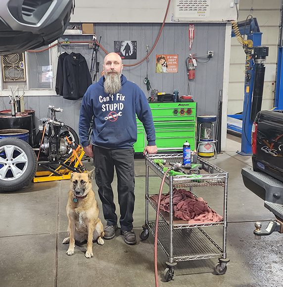 mechanic and a dog standing in an auto repair shop.
